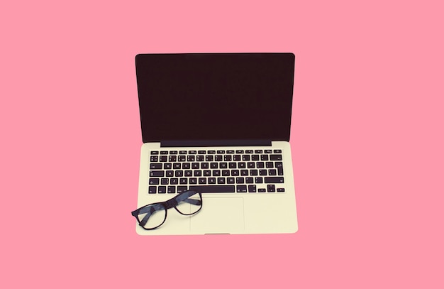 Bliski laptop z pustym czarnym ekranem i okularami na różowym tle