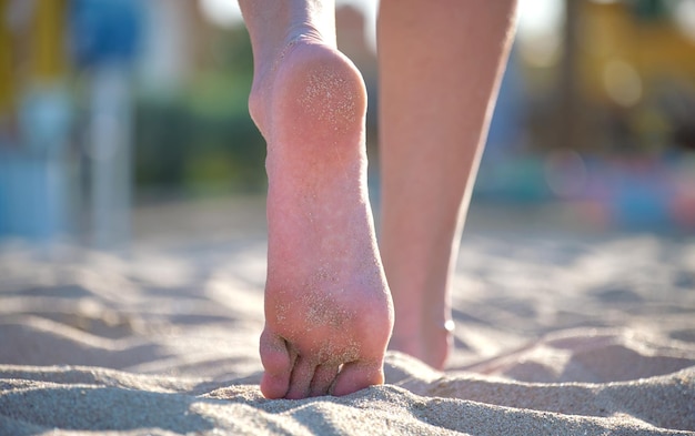 Bliskie zdjęcia stóp kobiet chodzących boso po białym ziarnistym piasku złotej plaży na niebieskim tle wody oceanu