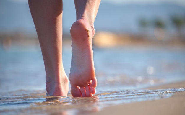 Blisko kobiecych stóp chodzących boso po białym ziarnistym piasku złotej plaży na niebieskim tle wody oceanu