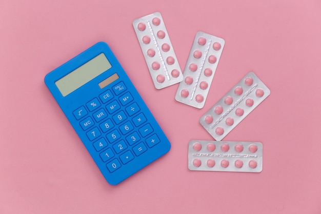 Blistry tabletek i kalkulatora na różowym tle. Widok z góry