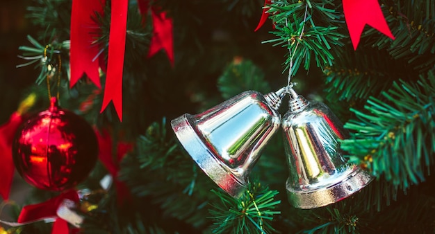 Bliźniacze srebrne dzwony i czerwona wstążka z czerwonymi bombkami zdobią choinkę bożonarodzeniową