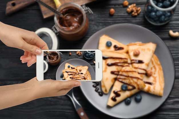 Bloger kulinarny robi zdjęcie pysznych cienkich naleśników przy drewnianym stole