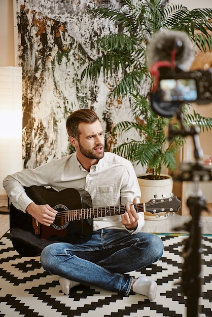 bloger muzyczny grający na gitarze i śpiewający podczas nagrywania nowego wideo dla swoich subskrybentów.