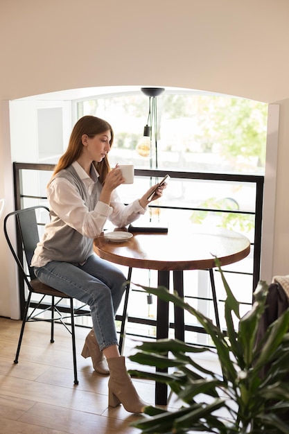 Blogerka w kawiarni przy oknie z kawą i smartfonem