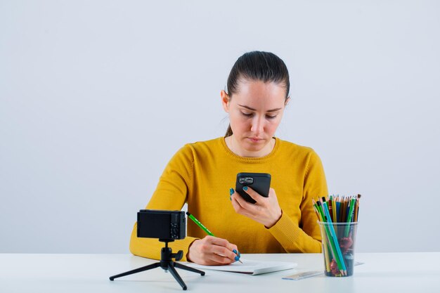 Blogger dziewczyna patrzy na telefon i pisze tekst, siedząc na białym tle