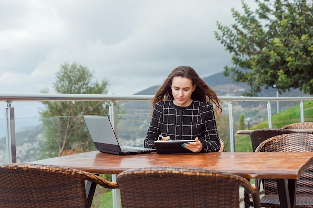 Blogger dziewczyna robi bloga na laptopie, siedząc na tle widoku natury