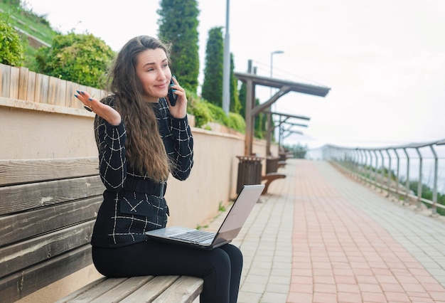 Blogger dziewczyna rozmawia przez smartfona, podnosząc rękę w parku