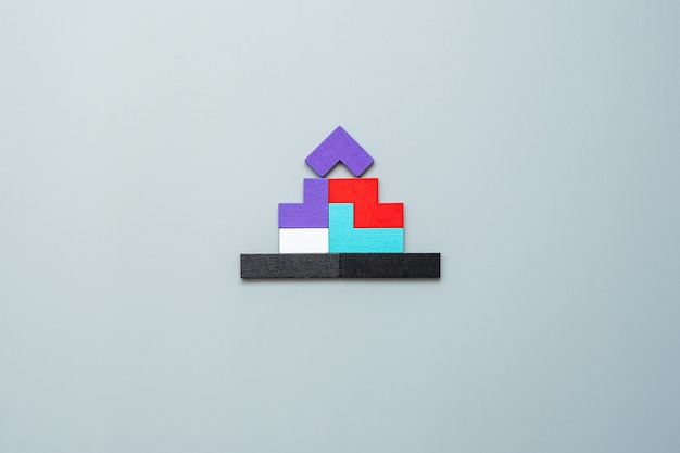 Zdjęcie blok w kształcie domu z kolorowymi drewnianymi puzzlami na szaro. logiczne myślenie, logika biznesowa, rozwiązania, koncepcje racjonalne, dom, nieruchomości i strategie