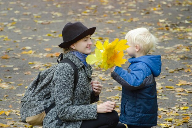 Zdjęcie blond chłopiec daje mamie bukiet żółtych liści jesienny las