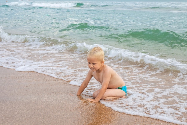 Blond chłopiec gra w fali morskiej na piaszczystej plaży Letnie wakacje