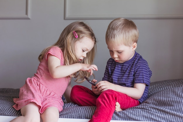 Blond Chłopiec I Dziewczynka Siedzą Na łóżku I Patrzą Na Smartfona Komunikacja Online Komunikacja Wideo Edukacja