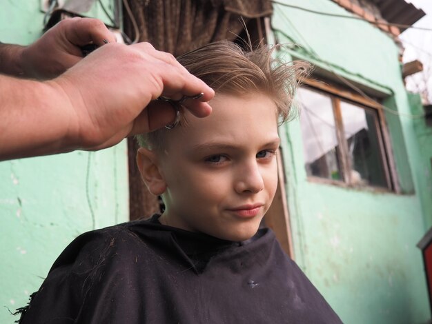 Blond Chłopiec W Wieku 8 Lat Obcina Włosy Nożyczkami Usługi Fryzjerskie W Domu Strzyżenie Dla Dziecka O Blond Włosach