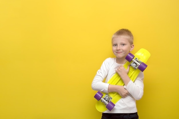 Blond chłopiec z niespodzianką i radością przytula deskorolkę na żółtym tle z miejsca na kopię prezent