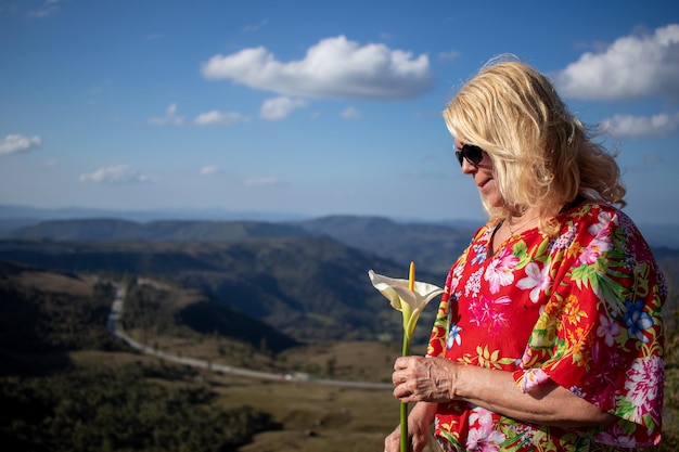 blond dama we wzorzystej bluzce i okularach przeciwsłonecznych trzymająca i patrząca na biały kwiat