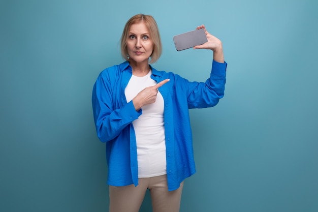 Zdjęcie blond dojrzała kobieta trzyma smartfona z makieta na czystym tle studia