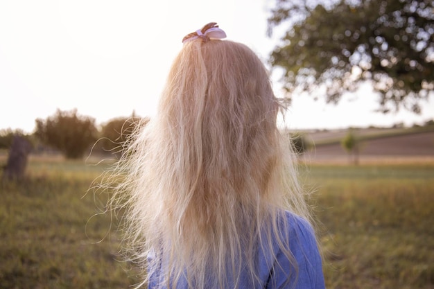 Blond dziewczynka z puszystymi włosami z plecami stoi na tle pola