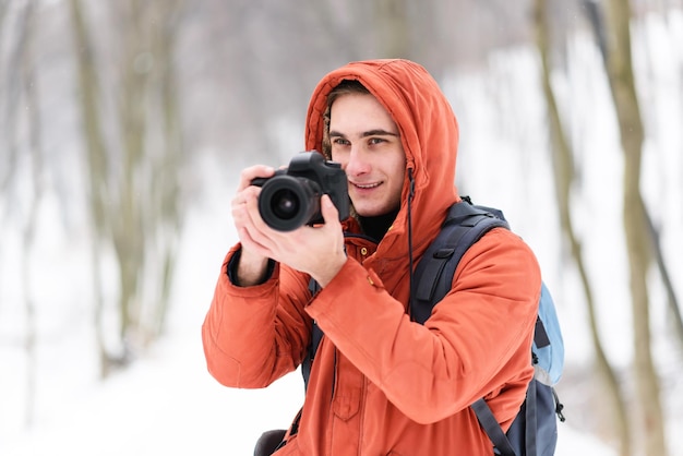 Blond fotografia chłopiec w kapturze stojący z aparatem na tle zimowego lasu