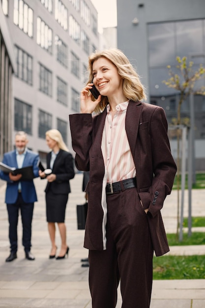 Blond kobieta stoi i rozmawia przez telefon przed nowoczesnym biurem