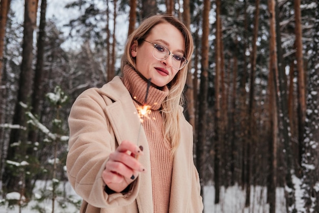 Blond kobieta w średnim wieku w zimowym lesie z brylantem w dłoni Kobieta w płaszczu i swetrze na zewnątrz