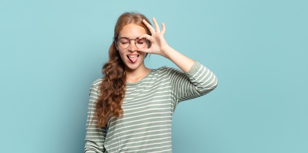 Blond ładna Kobieta Uśmiecha Się Radośnie Ze śmieszną Miną, żartuje I Patrzy Przez Wizjer, Szpieguje Sekrety