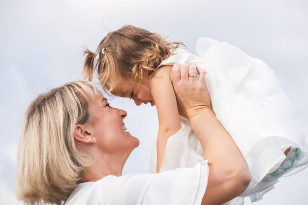 Blond mama trzyma córeczkę w parku latem przy słonecznej pogodzie