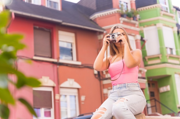 Blond turysta na ulicy z domami z kolorowymi fasadami siedzi i robi zdjęcie aparatem