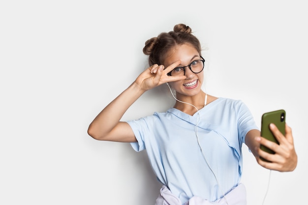 Blondynka Młoda Kobieta Uśmiecha Się I Robi Selfie Podczas Noszenia Okularów I Słuchawek Na Białej ścianie Studia Z Wolną Przestrzenią