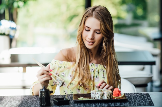 Blondynka, młoda piękna blond kobieta, studentka jedząca sushi na letnim tarasie w japońskiej restauracji