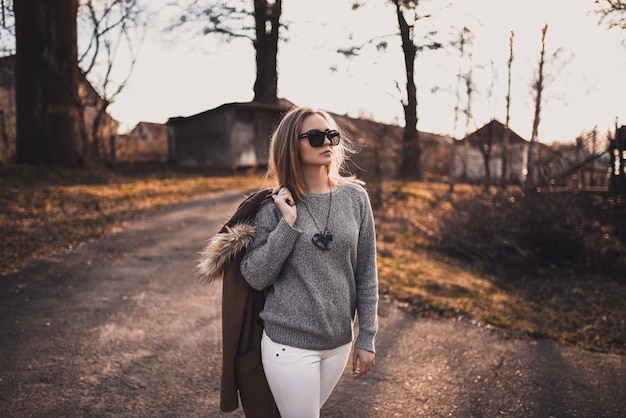 Blondynka modelka w białe spodnie, okulary przeciwsłoneczne, brązowy płaszcz