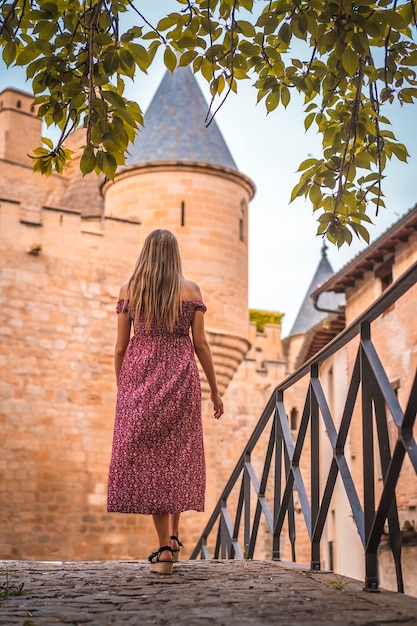 Blondynka obok średniowiecznego zamku z czerwoną sukienką od tyłu
