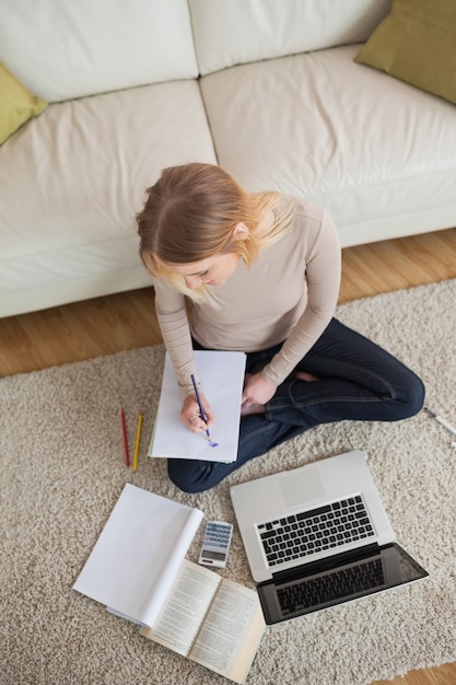 Blondynka robi praca domowa i obsiadanie na podłogowym używa laptopie