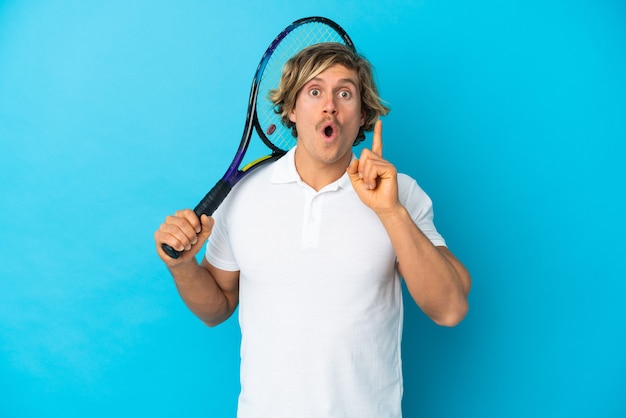 Blondynka tenisista mężczyzna na białym tle na niebieskiej ścianie zamierzający realizować rozwiązanie, podnosząc palec w górę