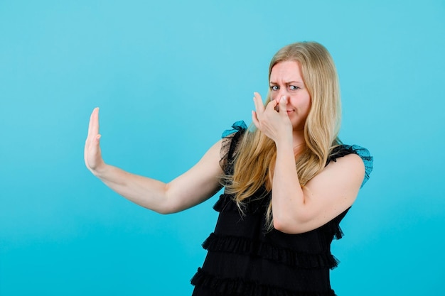 Zdjęcie blondynka trzyma nos i pokazuje gest stop na niebieskim tle