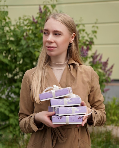 Zdjęcie blondynka w beżowym płaszczu trzyma cztery pudełka z prezentami