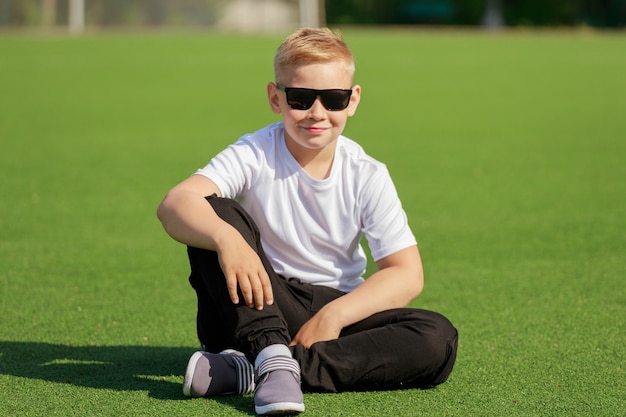 Blondynka w ciemnych okularach siedzi na boisku w lecie. Zdjęcie wysokiej jakości