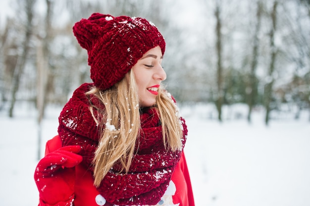 Blondynka w czerwony szalik, kapelusz i santas sweter pozowanie w parku na zimowy dzień.