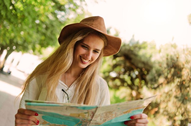 Blondynka w filcowym kapeluszu patrzy na mapę miasta i spaceruje po nieznanym mieście na świeżym powietrzu