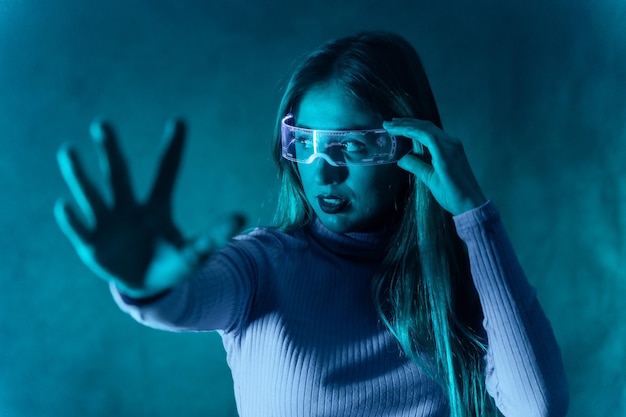 Blondynka w futurystycznych okularach gestykuluje na niebieskim tle wykonując gest zatrzymania