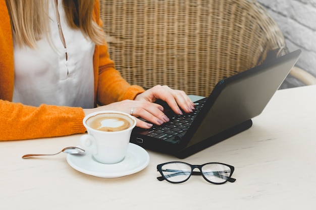 Blondynka w kawiarni z laptopem i kawą. Freelancer młoda dziewczyna pracuje na laptopie