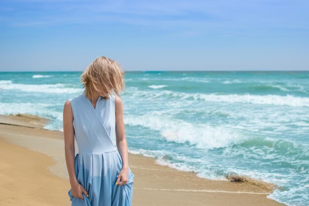 Blondynka w niebieskiej sukience nad brzegiem oceanu Pojęcie wakacji letnich podróży wakacyjnych