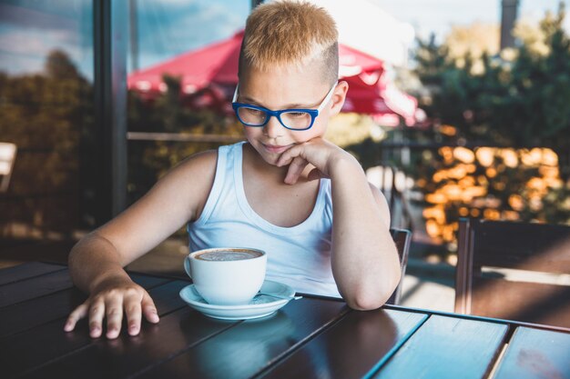 Blondynka w okularach siedzi w kawiarni i pije kawę