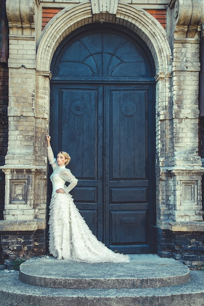 Blondynka w sukience retro na tle starych ciemnych drzwi budynku