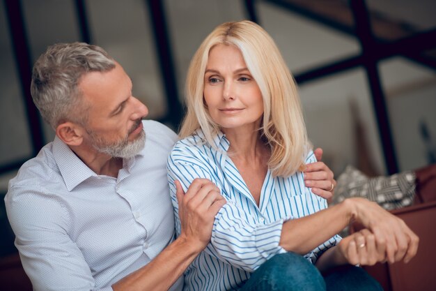 Blondynka wygląda smutno, jej mąż dotyka jej ramienia