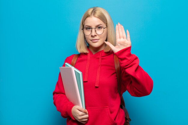 Blondynka wyglądająca poważnie, surowo, niezadowolona i wściekła pokazuje otwartą dłoń wykonującą gest stop