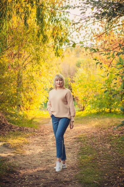 Blondynka z krótką fryzurą idzie przez las w sweterku z dzianiny. Wędrówki na świeżym powietrzu w jesiennym lesie