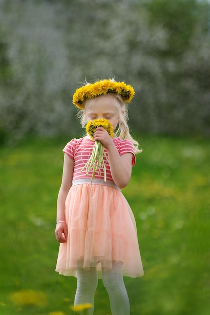 Zdjęcie blondynka z kwiatami mniszka lekarskiego dziecko w wieńcu kwiatów pachnie bukietem mniszka lekarskiego selektywna ostrość