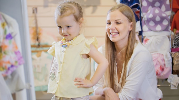 Zdjęcie blondynka z małą córeczką kupuje dziecięcą sukienkę w sklepie z ubraniami