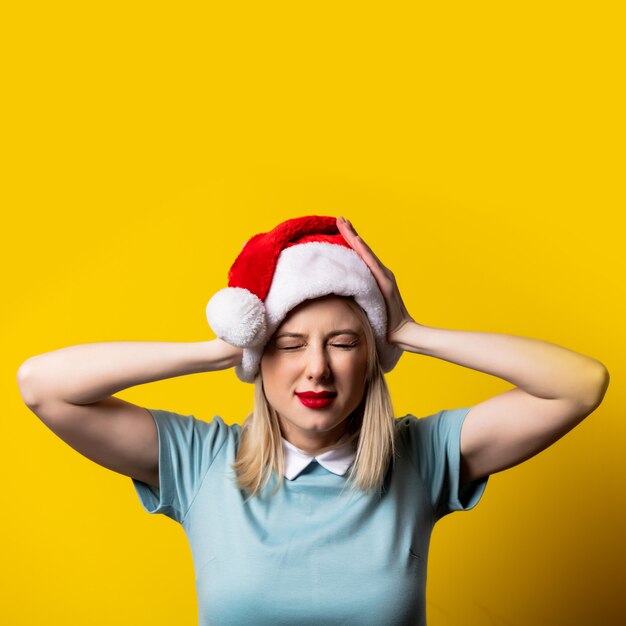 Blondynki dziewczyna w błękit sukni i Święty Mikołaj kapeluszu na kolor żółty przestrzeni