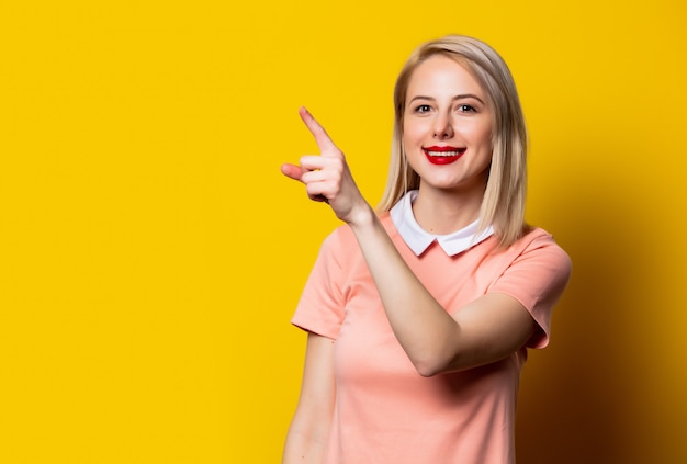 Blondynki dziewczyna w menchii sukni przedstawienia gescie na kolor żółty przestrzeni