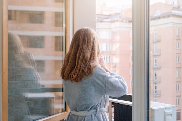 Blondynki kobieta pije jej ranek kawę lub herbaty na śródmieściu balkonie w szlafroku